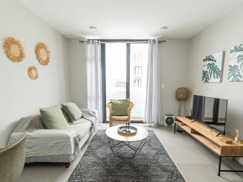 A bright and modern living room featuring neutral tiled flooring and a large sliding glass door providing access to the balcony.