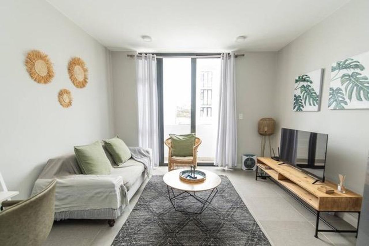 A bright and modern living room featuring neutral tiled flooring and a large sliding glass door providing access to the balcony.