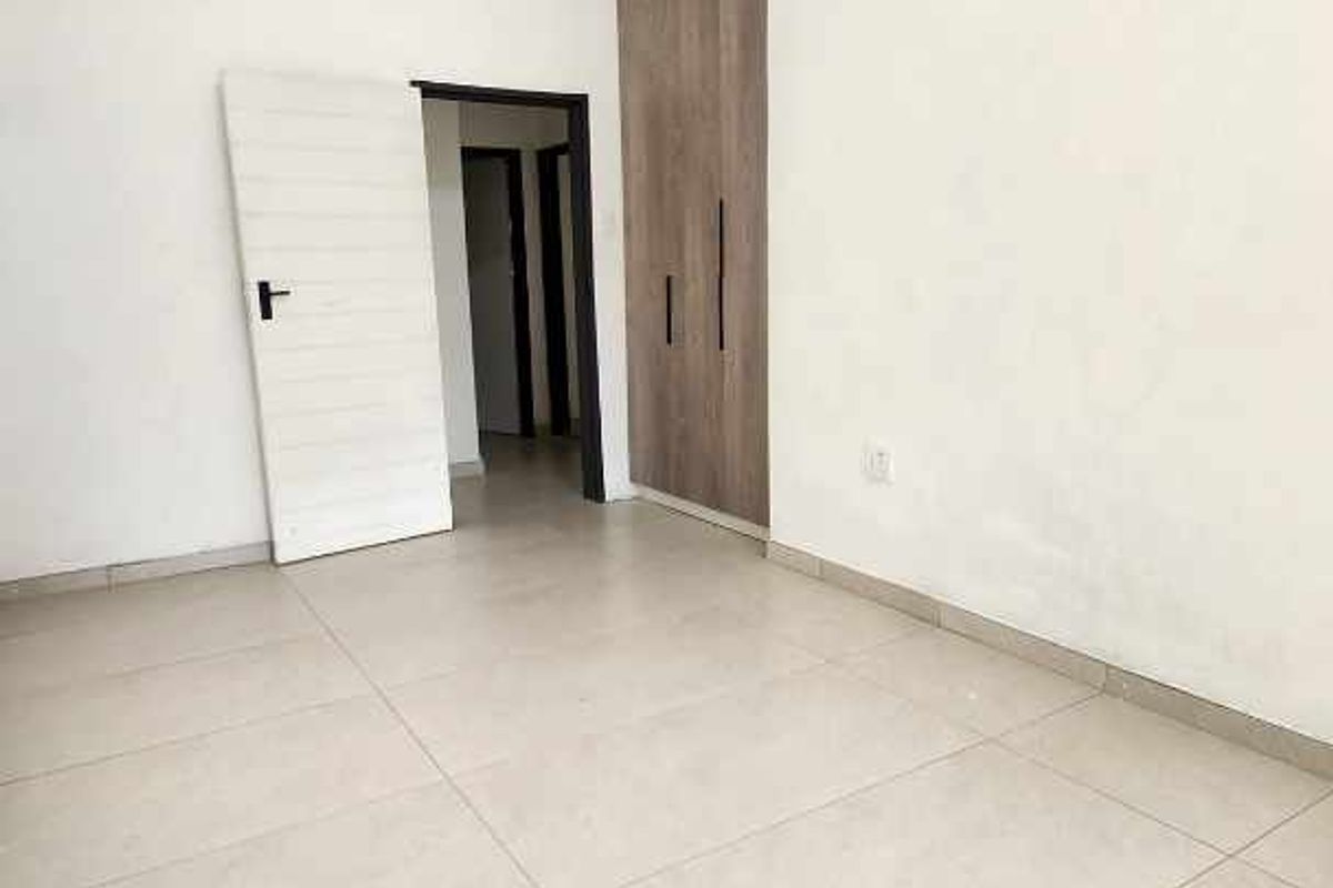 A bright, empty bedroom featuring large format floor tiles, a built-in wooden wardrobe, and recessed ceiling lighting.