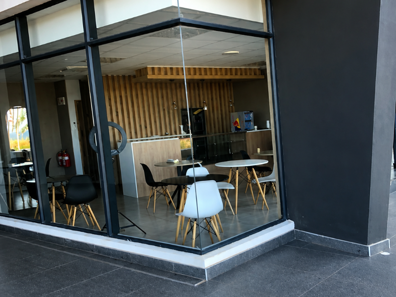 A modern retail storefront featuring a large glass corner facade, timber slat wall detailing, and clean tiled exterior flooring.