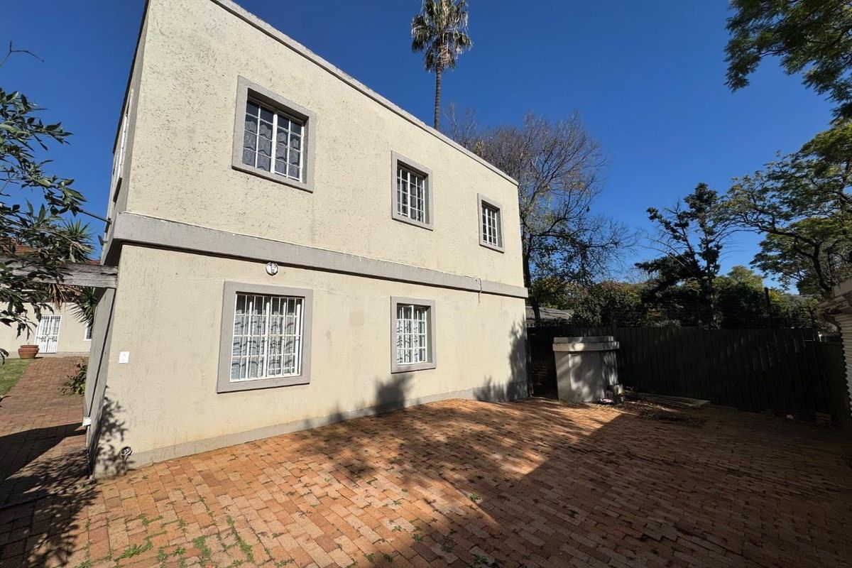 A two-story exterior rear view of the house featuring a paved courtyard area, security bars on windows, and a concrete water tank.