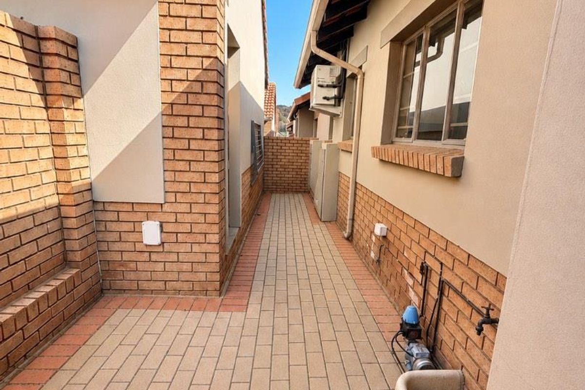 A paved side walkway or utility area featuring brick walls, an external water tap, a utility sink, and a water pump installation.