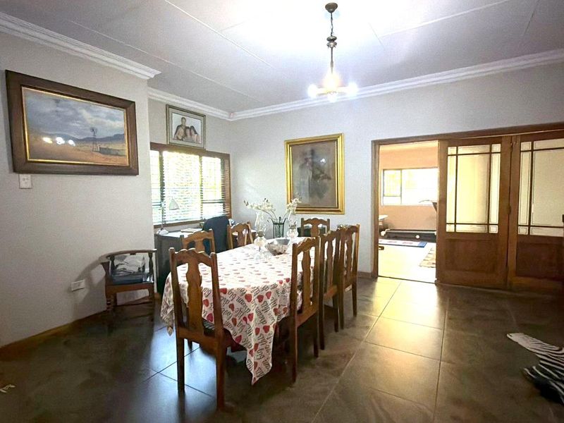 A spacious dining room featuring tiled flooring, crown molding, and sliding wooden doors leading to an adjacent room.