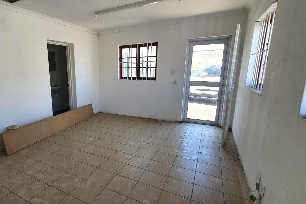 An empty, tiled living area featuring security bars on windows and direct access to an adjacent bathroom.