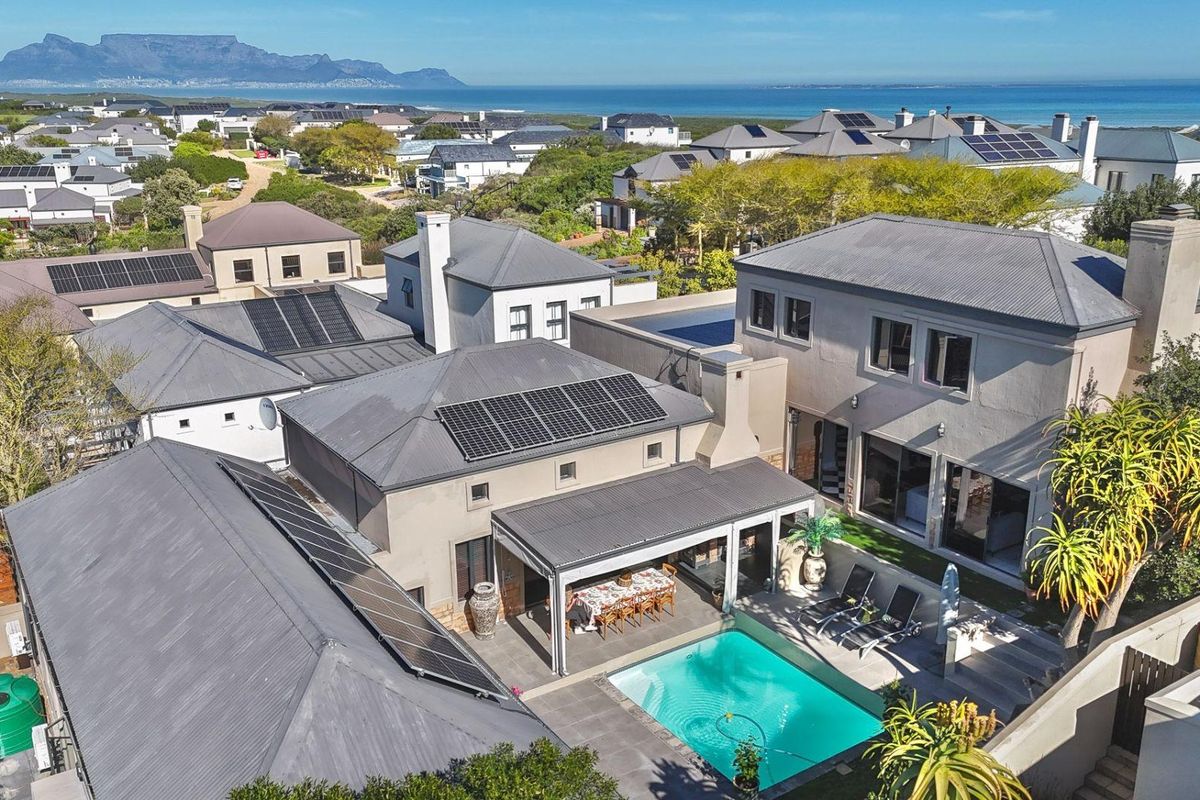 Aerial view of a residential property featuring a swimming pool, covered patio, and solar panel installation, set within a coastal estate.