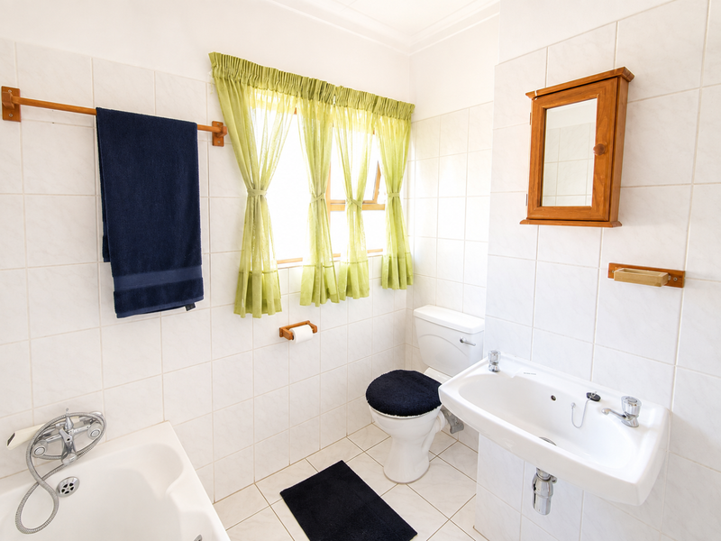 A functional bathroom featuring a bathtub, wall-mounted basin, toilet, and tiled finishes, offering a clean and practical layout.