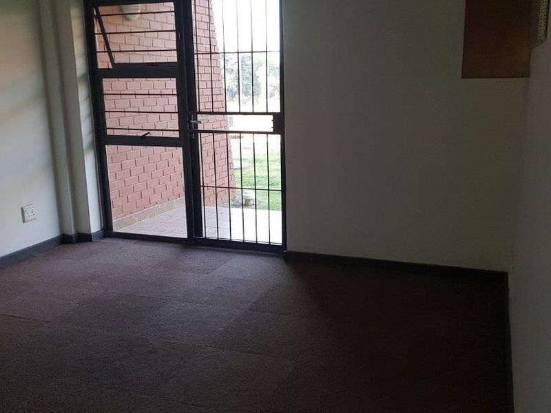 An empty living room featuring carpet flooring and a sliding glass door with an integrated security gate leading to an outdoor area.