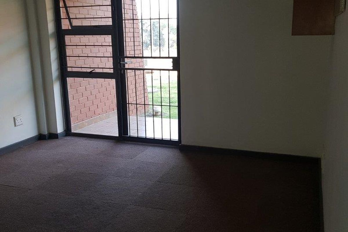 An empty living room featuring carpet flooring and a sliding glass door with an integrated security gate leading to an outdoor area.