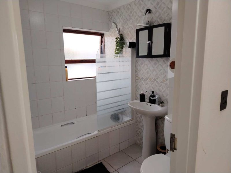 A compact bathroom featuring a pedestal basin, bathtub with a glass shower screen, and tiled finishes throughout.