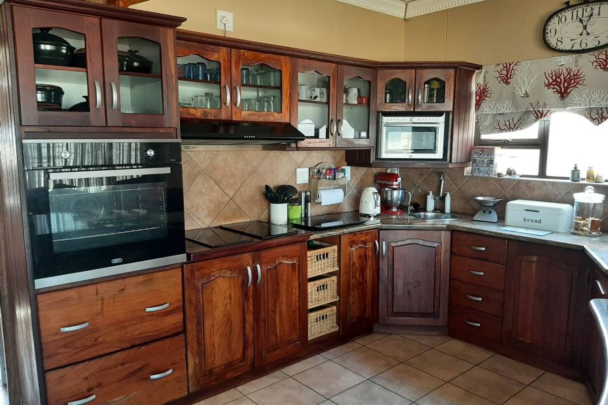 A functional kitchen featuring dark wood cabinetry, built-in oven, extractor fan, and tiled flooring, offering a classic aesthetic with ample storage space.