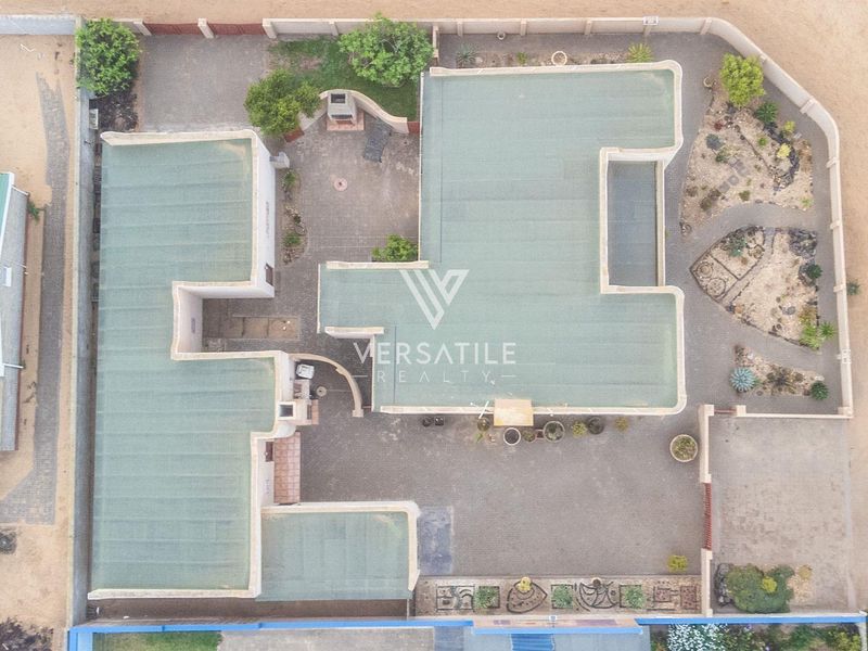 Aerial view of the property showcasing the flat roof structure, paved courtyard area with built-in braai, and surrounding landscaped garden within boundary walls.