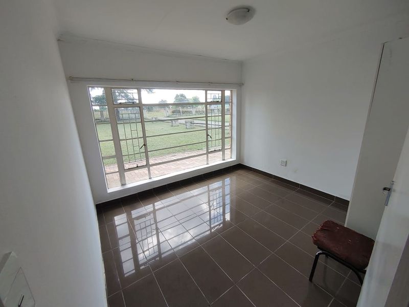 A vacant bedroom featuring large steel-framed windows, tiled flooring, and a built-in cupboard, offering a view of the garden.