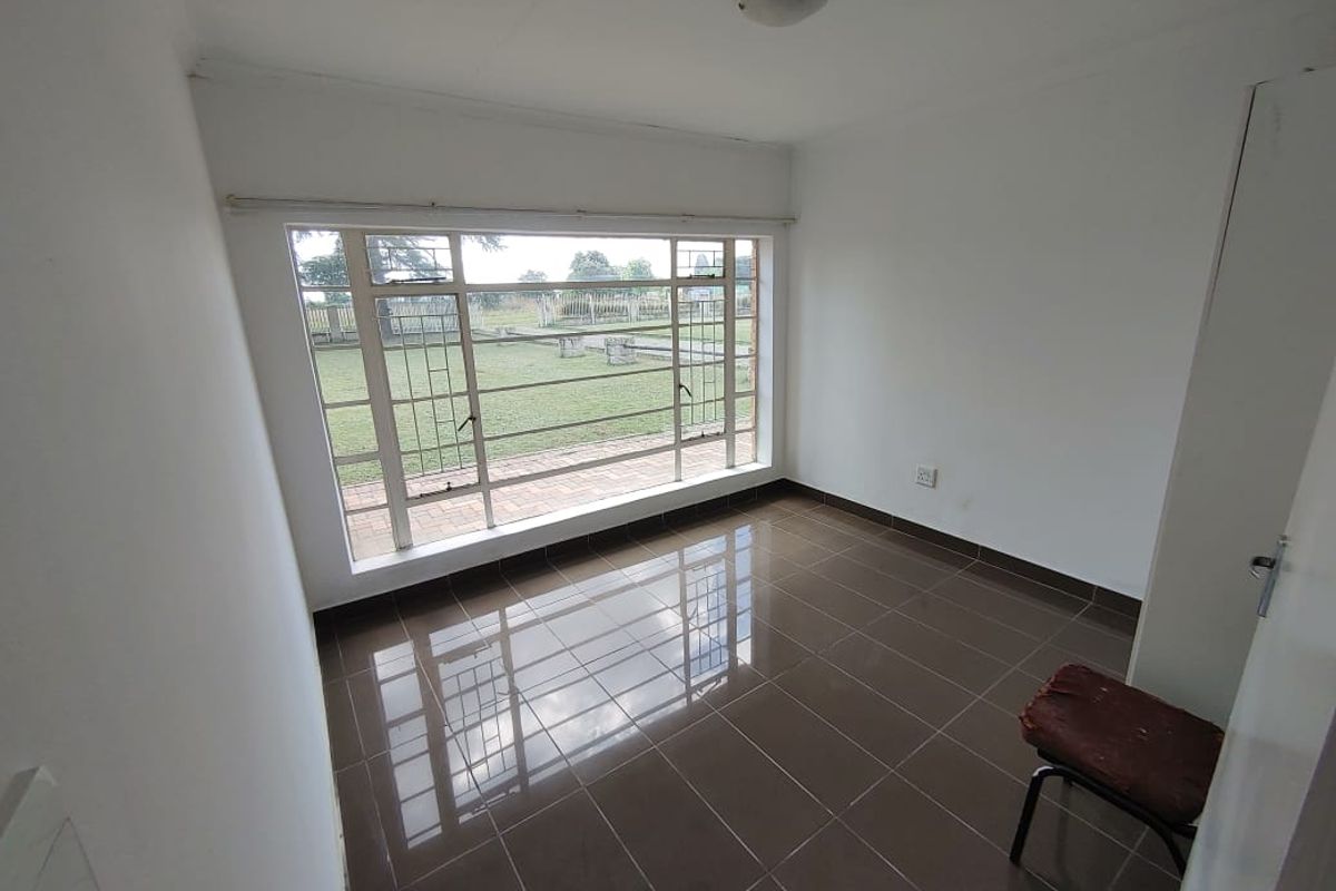 A vacant bedroom featuring large steel-framed windows, tiled flooring, and a built-in cupboard, offering a view of the garden.