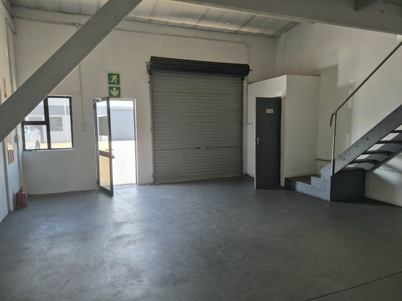 Open plan industrial utility space featuring concrete flooring, exposed steel structural elements, a roller shutter door, and an internal staircase leading to an upper level.