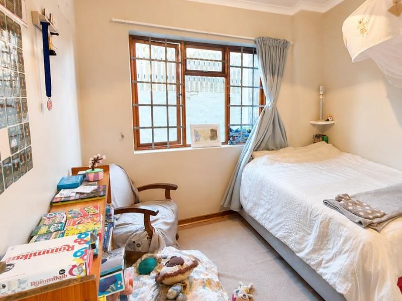 A cozy bedroom featuring carpeted flooring, a timber-framed window with security bars, and classic cove cornicing.