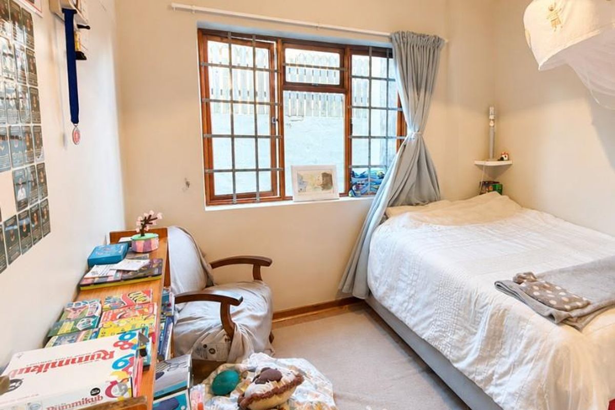 A cozy bedroom featuring carpeted flooring, a timber-framed window with security bars, and classic cove cornicing.