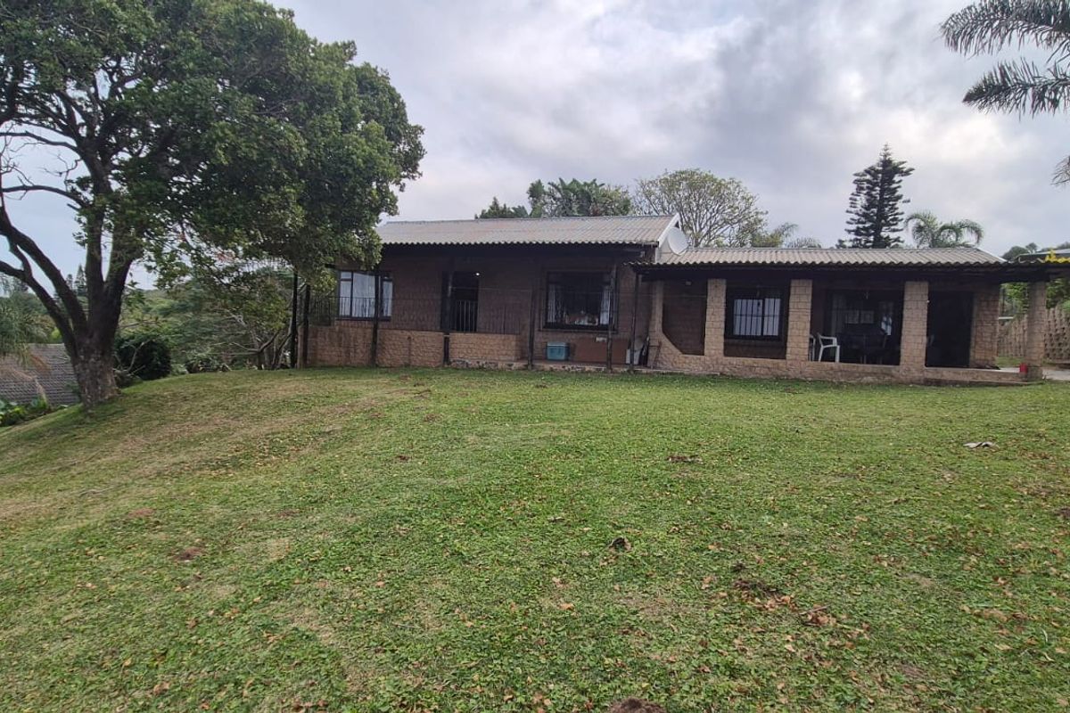 A rear view of the house featuring a brick facade, a covered patio area, and a large sloping lawn.