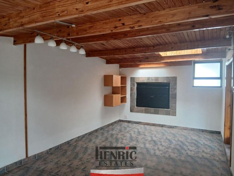 Spacious living area featuring an exposed timber beam ceiling, built-in fireplace with tiled surround, and natural light from a skylight.