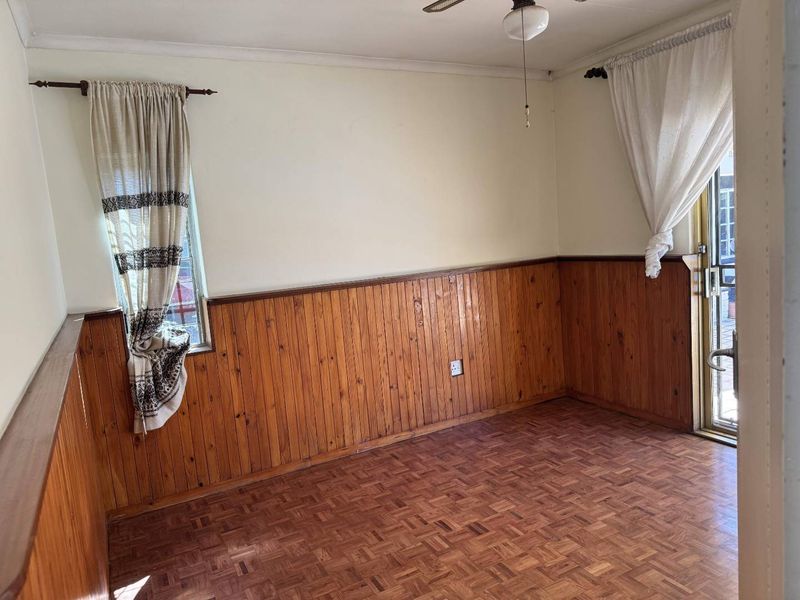 An empty living room featuring traditional timber wall paneling, parquet flooring, and a ceiling fan, with direct access to an outdoor area via a sliding door.