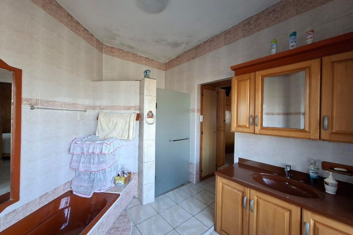 A dated bathroom featuring a built-in vanity, integrated sink, tiled walls, and a built-in bathtub with shower enclosure.