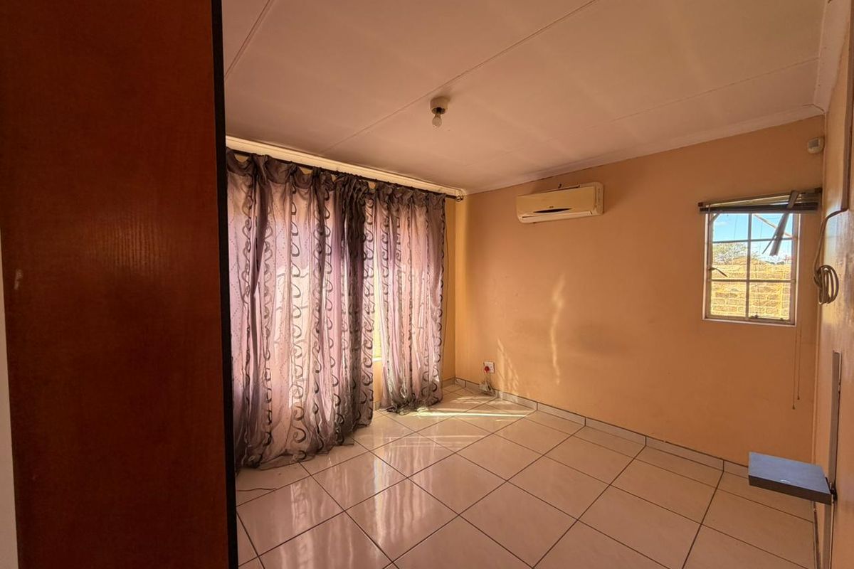 A bedroom featuring tiled flooring, a wall-mounted air conditioning unit, and large windows with curtains.