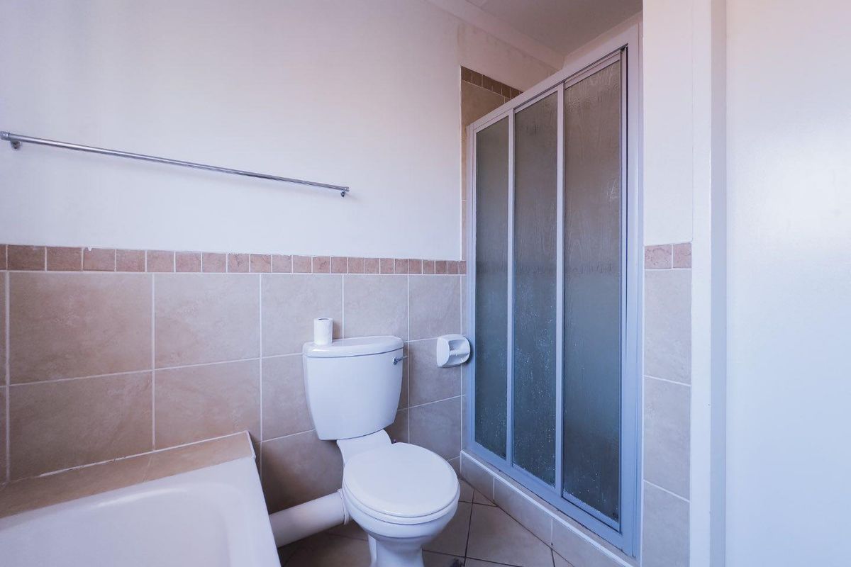 A functional bathroom featuring a shower enclosure, a standard toilet, and neutral wall tiling.