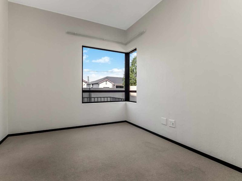 A bright, empty bedroom featuring neutral walls, carpeted flooring, and a corner window that provides natural light.