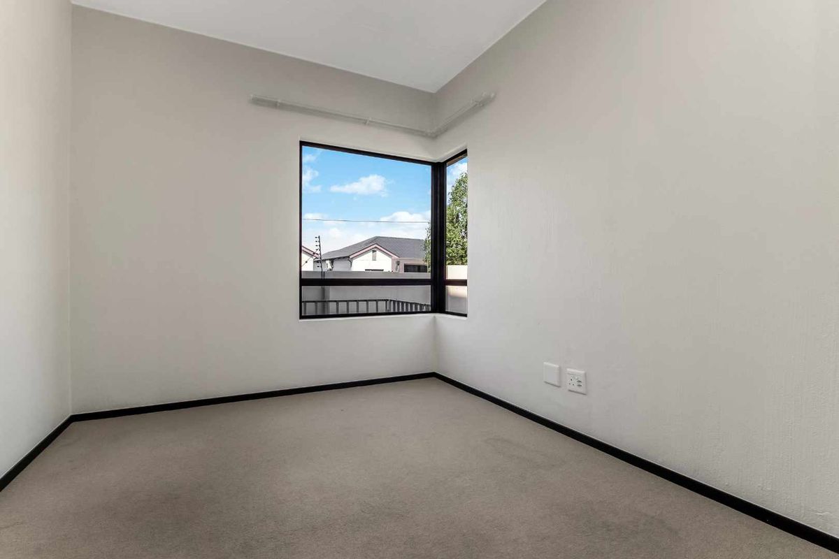 A bright, empty bedroom featuring neutral walls, carpeted flooring, and a corner window that provides natural light.