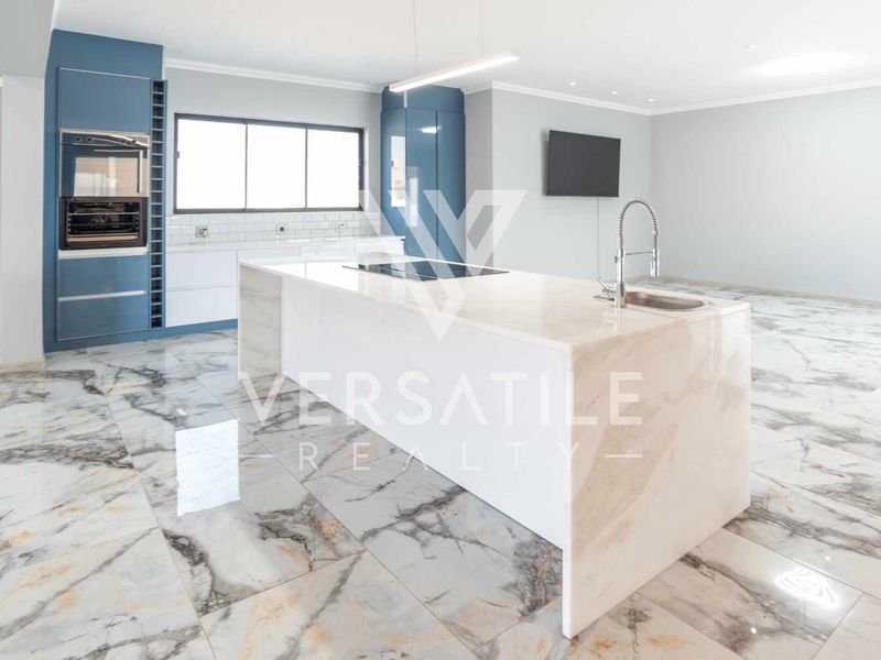 Modern open-plan kitchen featuring a large marble-look island, built-in oven, sleek blue cabinetry, and polished marble-look floor tiles throughout the spacious living area.