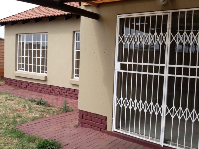 Rear exterior view of the townhouse featuring a covered patio area with brick paving, security gates, and a tiled roof structure.