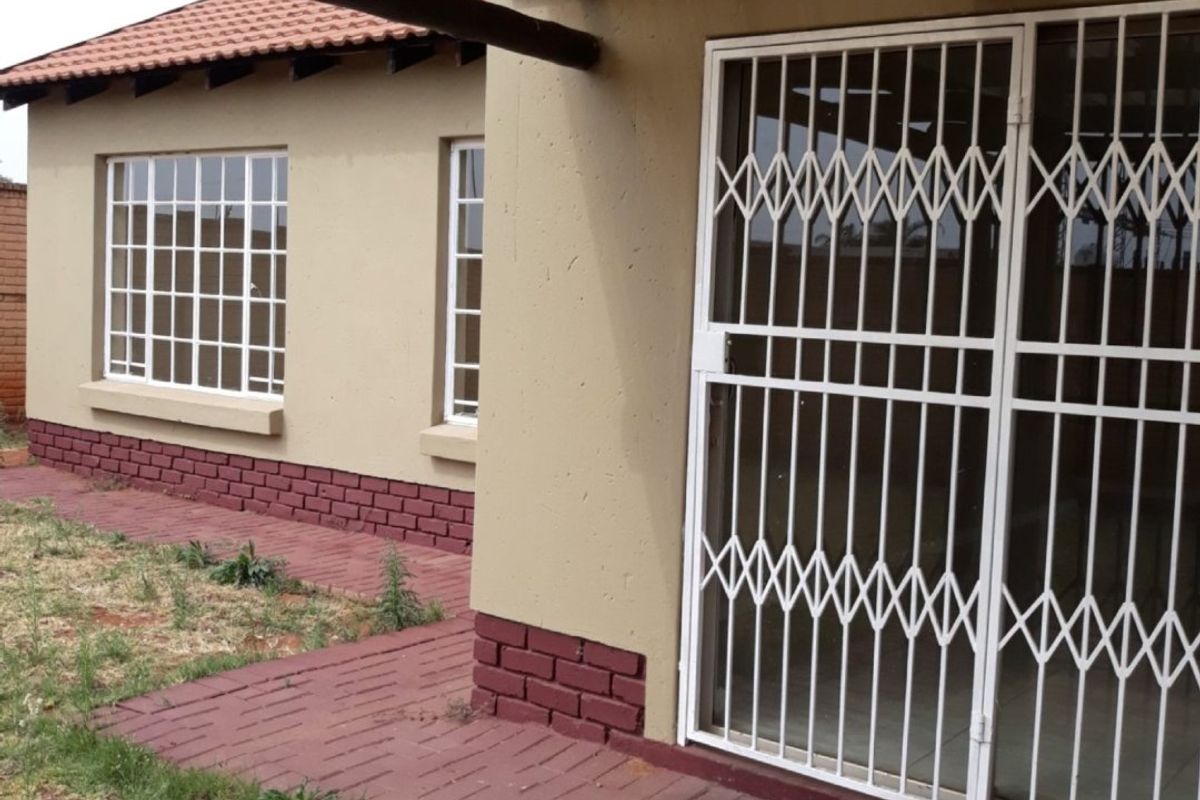 Rear exterior view of the townhouse featuring a covered patio area with brick paving, security gates, and a tiled roof structure.