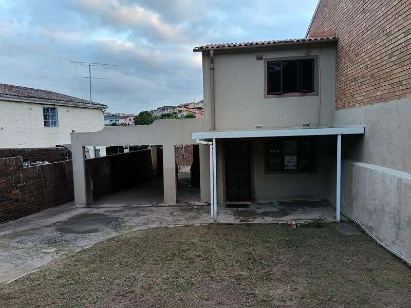 Rear view of the property featuring a covered patio area, attached carport, and a small garden space with concrete paving.