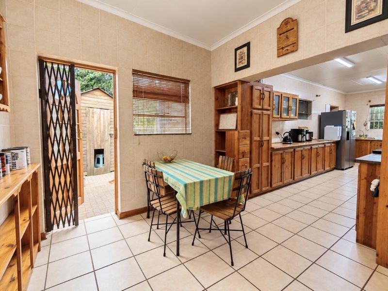 Open-plan kitchen and dining area featuring tiled flooring, extensive wooden cabinetry, and direct access to the exterior through a security gate.