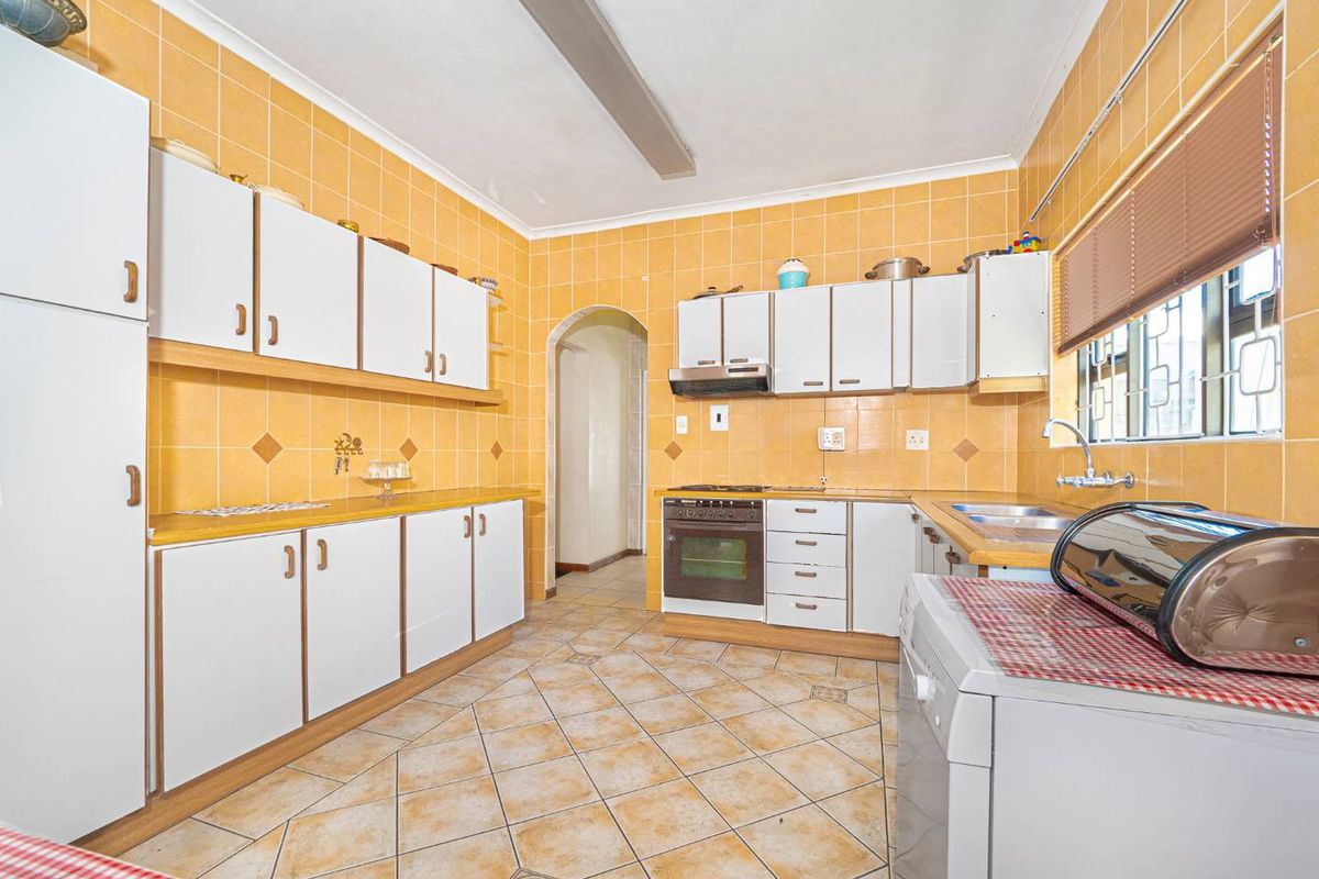 A functional kitchen featuring extensive built-in cabinetry, tiled splashbacks, and tiled flooring, equipped with a built-in oven and extractor fan.