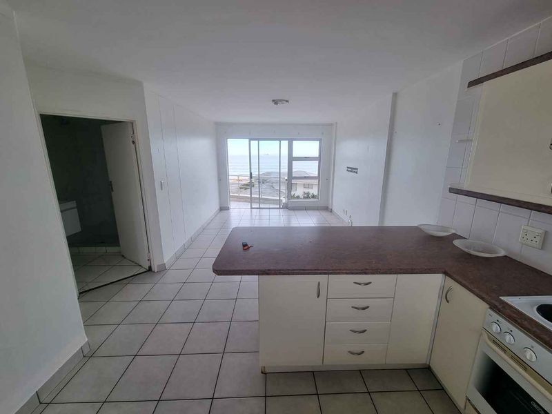 Open-plan living and kitchen area featuring tiled floors, built-in cabinetry, and a sliding door leading to a balcony with ocean views.