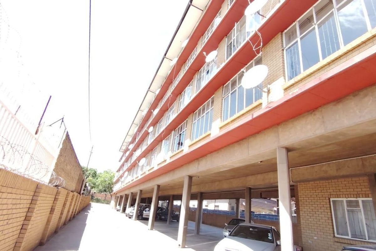 Exterior view of a multi-story apartment building featuring a ground-level covered parking area and brick facade construction.