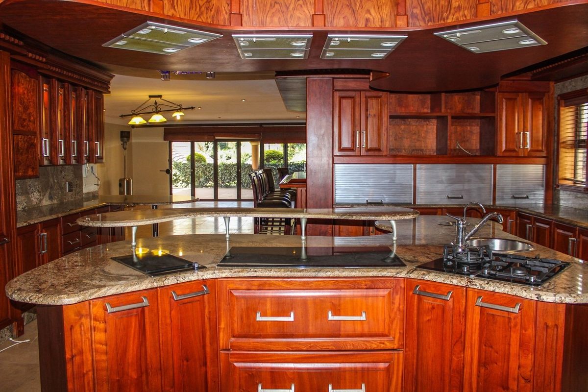 Spacious kitchen featuring extensive wooden cabinetry, granite countertops, a breakfast bar, and integrated gas cooktop, flowing into an open-plan living area.