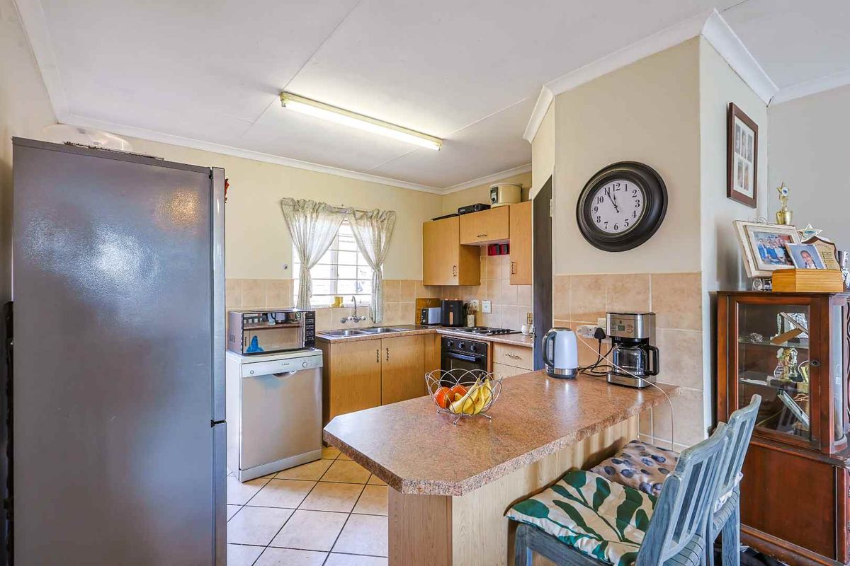 A functional kitchen featuring wooden cabinetry, a breakfast bar, tiled flooring, and a built-in oven with hob.