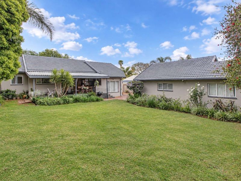 A well-maintained rear exterior view featuring a spacious lawn, landscaped garden beds, and a covered patio area attached to the main dwelling.