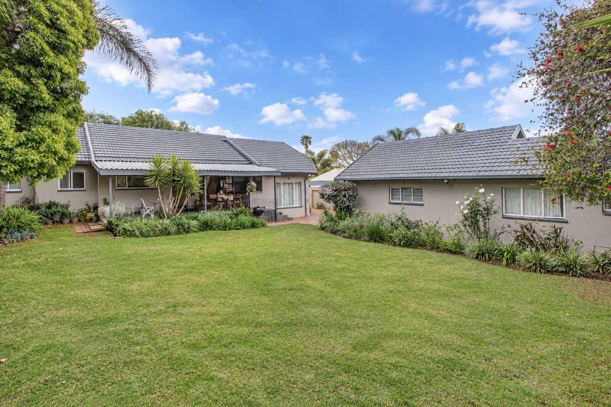 A well-maintained rear exterior view featuring a spacious lawn, landscaped garden beds, and a covered patio area attached to the main dwelling.