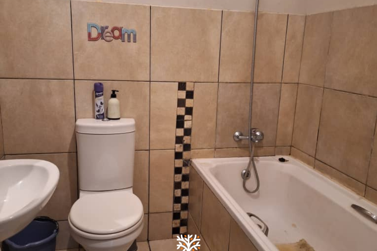 A functional bathroom featuring a standard bathtub with shower attachment, a pedestal basin, and a toilet, finished with neutral wall tiling.