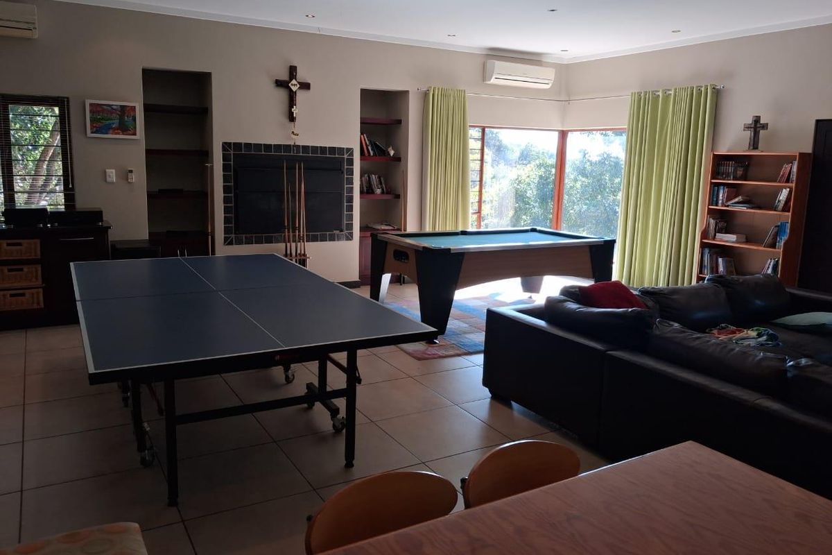 Spacious living area featuring tiled flooring, built-in shelving, a fireplace, and wall-mounted air conditioning unit, suitable for a games room or lounge.