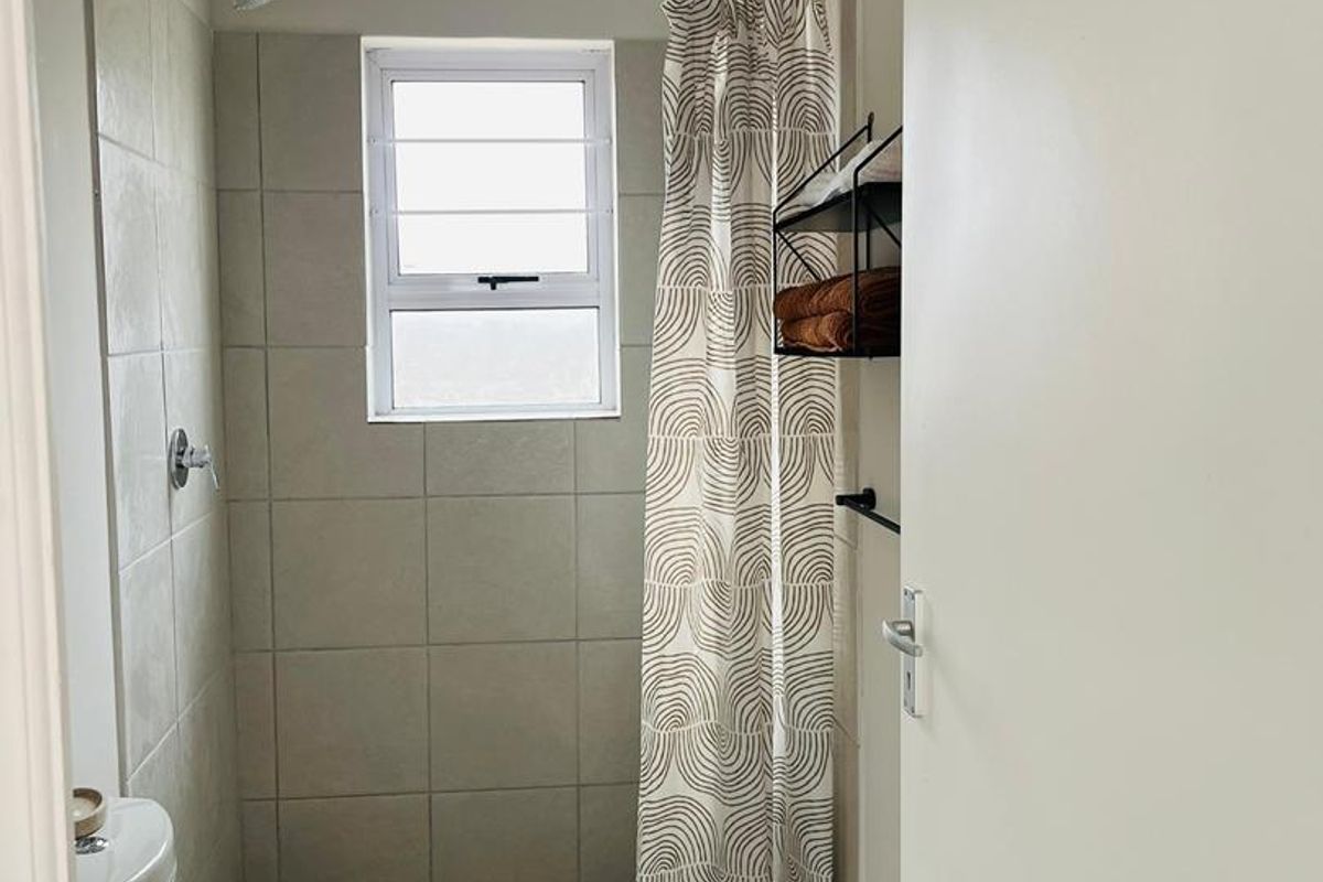 A functional bathroom featuring a shower with tiled surround, a louver window for ventilation, and a standard toilet.