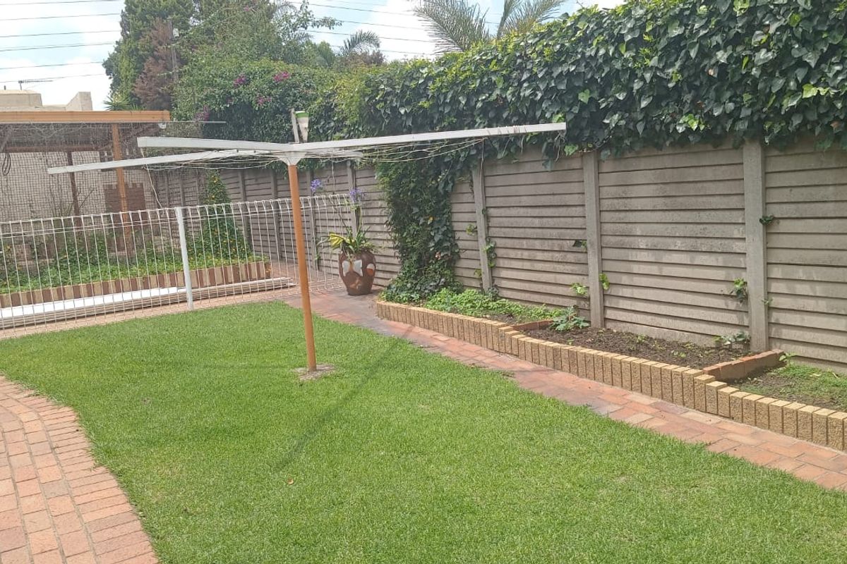 A private rear garden featuring a manicured lawn, brick-paved pathways, raised garden beds, and a secure boundary wall with climbing ivy.