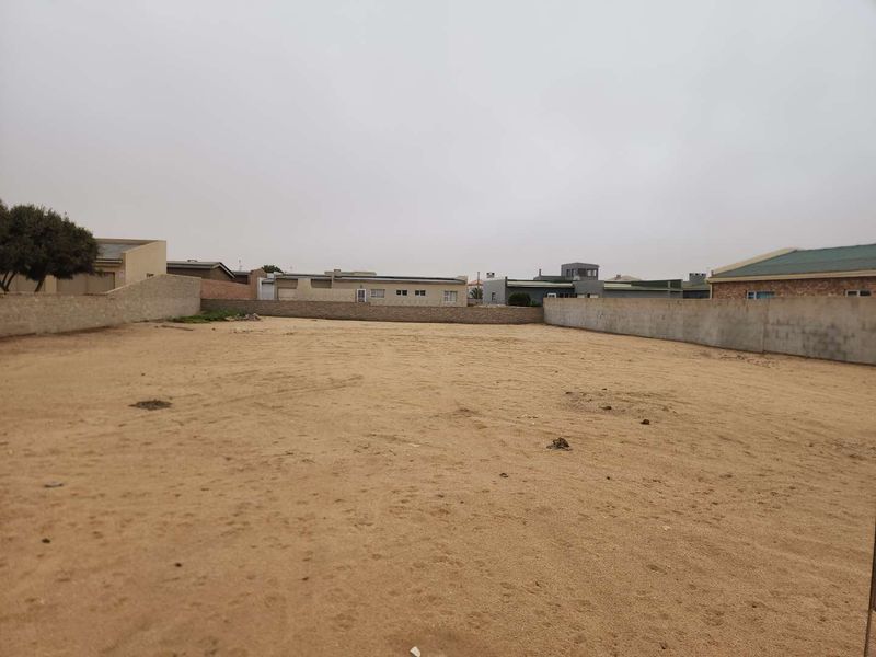 A vacant residential plot featuring a sandy surface enclosed by perimeter boundary walls, situated within an established neighborhood.