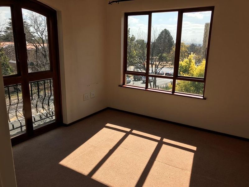 A bright, empty bedroom featuring carpeted flooring, large timber-framed windows, and a balcony door with wrought iron detailing, offering pleasant natural light.