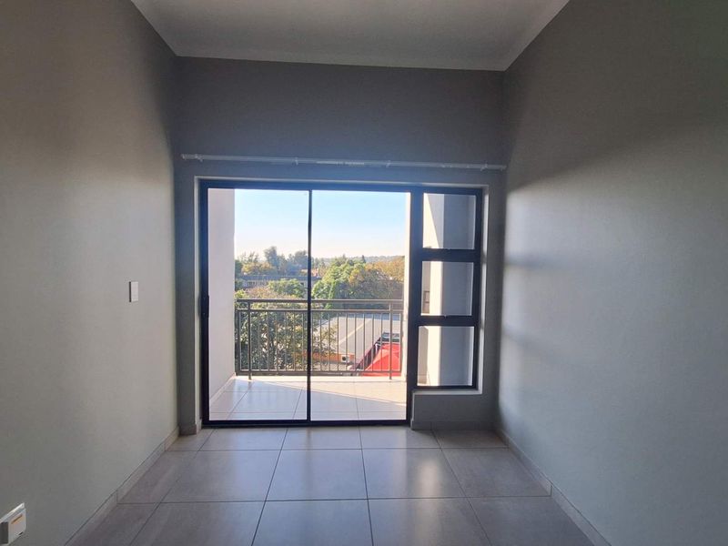 An empty, well-lit living area featuring neutral tiled flooring and a large sliding glass door providing access to a private balcony.