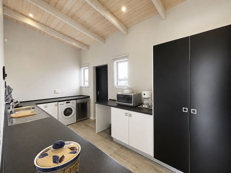 A modern, well-lit laundry room featuring sleek black and white cabinetry, a stainless steel sink, and exposed timber ceiling beams.