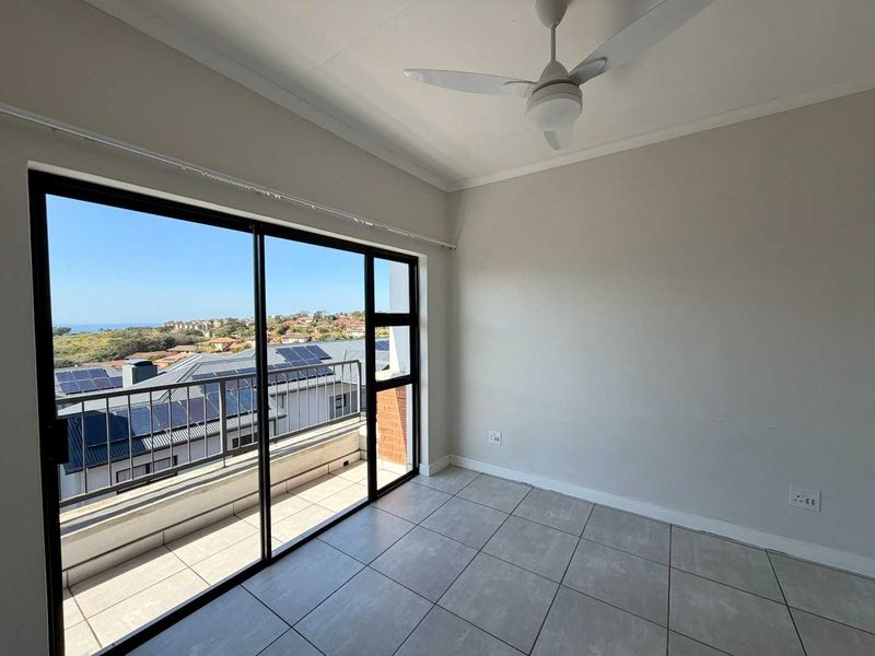 An empty bedroom featuring tiled flooring, a ceiling fan, and large sliding glass doors that open onto a balcony with scenic views.