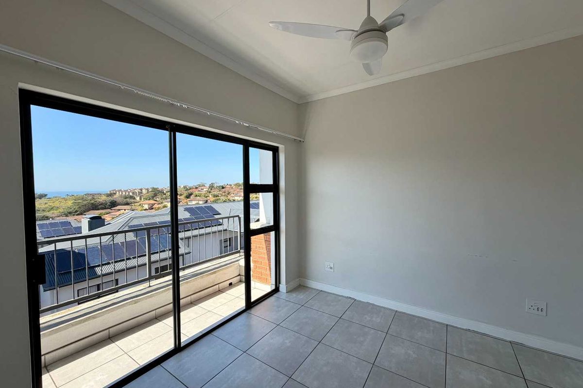 An empty bedroom featuring tiled flooring, a ceiling fan, and large sliding glass doors that open onto a balcony with scenic views.